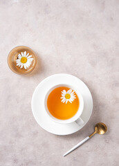 chamomile tea in a white cup with flowers and a vase on a pink-gray background. Top view and copy space