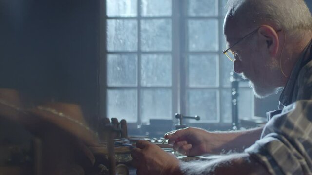Footage of goldsmith working at table in workshop . Bearded old man jeweler creating new jewelry . Master goldsmith working process . Scenic film shot in vintage style. Shot on RED EPIC Camera.   