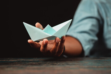A businessman holding a paper boat makes an origami boat out of banknotes. Freight Forwarding...