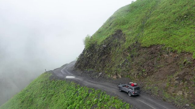 Cinematic drone shot of vehicle driving on the edge of a cliff on the Road to Tusheti going through puddles, one of the worlds most dangerous roads