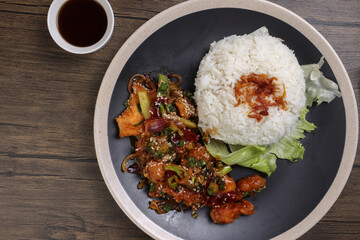 Chinese style Kung Pao Gong Bao Kung Po stair fried chicken with steamed rice lettuce on dark plate sauce fork spoon on rustic dark wood table
