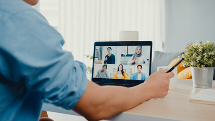 Young Asia businessman using laptop talk to colleagues about plan in video call meeting while work from home at living room. Self-isolation, social distancing, quarantine for corona virus prevention.