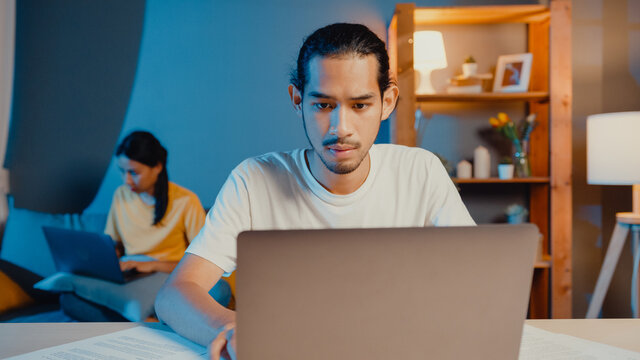 Freelance Asia Couple Man And Woman In Casual Feel Serious Focus On Work Separate Laptop Computer At Night, Hasband Sit In Front On Table Wife Sit Behind On Couch At House. Work From Home Concept.