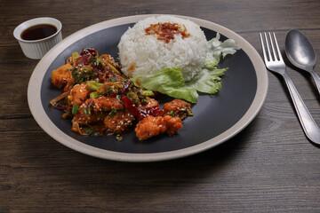 Chinese style Kung Pao Gong Bao Kung Po stair fried chicken with steamed rice lettuce on dark plate sauce fork spoon on rustic dark wood table