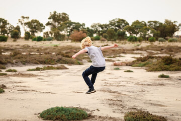 Little boy jumping in the air while exploring dry lake in the Australian bush