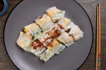 Chinse steamed rice noodle roll cheung fun stuffed shrimp prawn chicken vegetable fried onion garnish on dark plate sauce chopsticks on rustic dark wood table