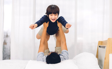 Fototapeta na wymiar Portrait of enjoy happy love asian family father carrying little asian boy son smiling playing superhero and having fun moments good time on bed at home