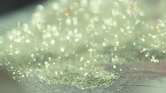 4K Close up of many silver glitters moving by wind . Real silver, golden or diamond dust blow . Abstract defocused bokeh crystal elements or sand on black background