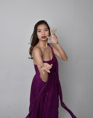 Close up portrait of pretty brunette asian girl wearing purple flowing  gown. Gestural hand movements on grey studio background.