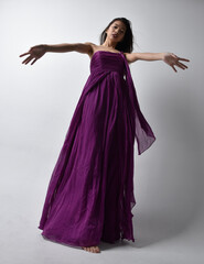 Full length  portrait of pretty brunette asian girl wearing purple flowing  gown. Standing pose in low angle on on studio background.