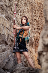 A model in an Indian costume with a bow for shooting stands among the rocks