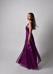 Obraz na płótnie Canvas Full length portrait of pretty brunette asian girl wearing purple flowing gown. Standing, dancing pose on on studio background.