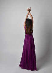 Full length  portrait of pretty brunette asian girl wearing purple flowing  gown. Standing, dancing...