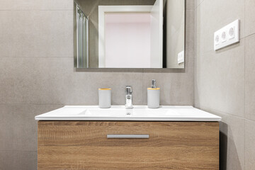 Close-up of white sink with modern wooden base and mirror in refurbished bathroom.