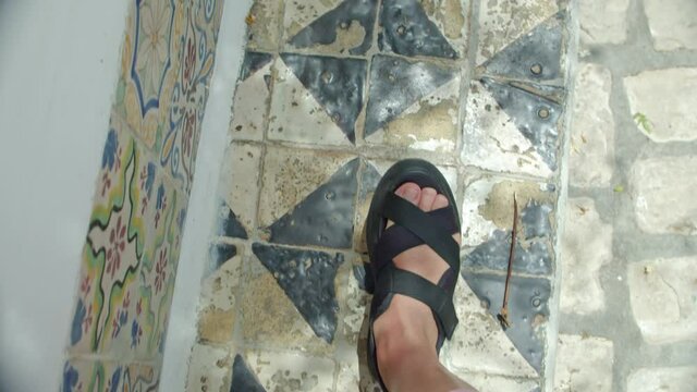 women's feet in black fashionable sandals are walking along the road of the old city paved with tiles with a beautiful ornament.