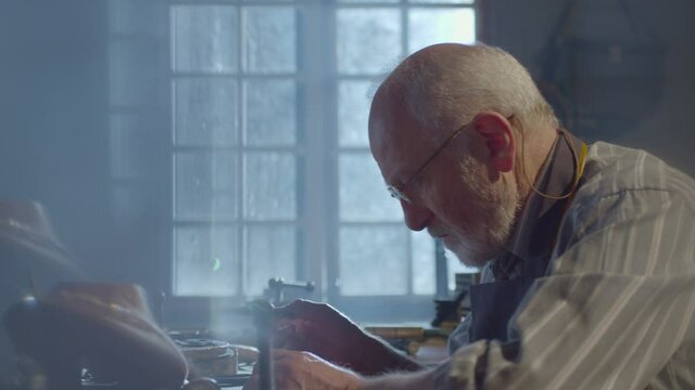 Footage of goldsmith working at table in workshop . Bearded old man jeweler creating new jewelry . Master goldsmith working process . Scenic film shot in vintage style. Shot on RED EPIC Camera.   