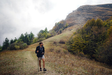 Fototapeta premium man with backpack and sticks for trekking hiking in the mountains. The beginning of autumn season. Beautiful foggy weather