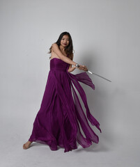 Full length  portrait of pretty brunette asian girl wearing purple flowing  gown. Sitting pose...