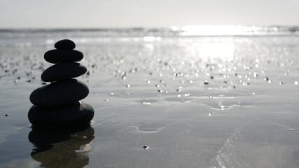 Fototapeta na wymiar Rock balancing on ocean beach, stones stacking by sea water waves. Pyramid of pebbles on sandy shore. Stable pile or heap in soft focus with bokeh, close up. Seamless looped cinemagraph. Zen balance.