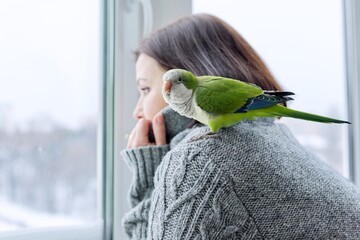 Winter, home lifestyle, woman and parrot looking together through the snowy window