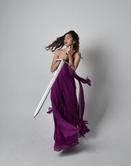 Full length  portrait of pretty brunette asian girl wearing purple flowing  gown. Sitting pose...