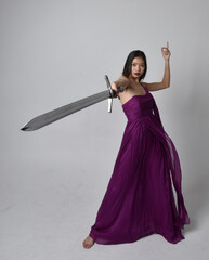 Full length  portrait of pretty brunette asian girl wearing purple flowing  gown. Sitting pose...