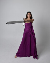 Full length  portrait of pretty brunette asian girl wearing purple flowing  gown. Sitting pose...