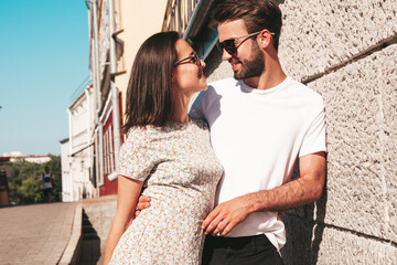 Naklejka premium Smiling beautiful woman and her handsome boyfriend. Woman in casual summer clothes. Happy cheerful family. Female having fun. Couple posing on the street background in sunglasses.Hugging each other