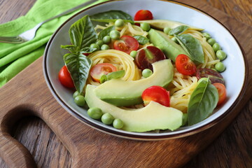 Pasta salad with green peas, avocado, cherry tomatoes and basil on rustic wooden background. Top view