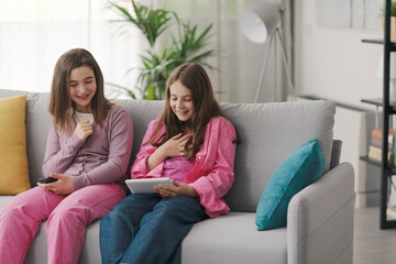 Happy girls sitting on the sofa and connecting with a digital tablet