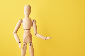 Wooden doll with gesture on yellow background. Mannequin shows gesture. Figure of wooden human with copy space