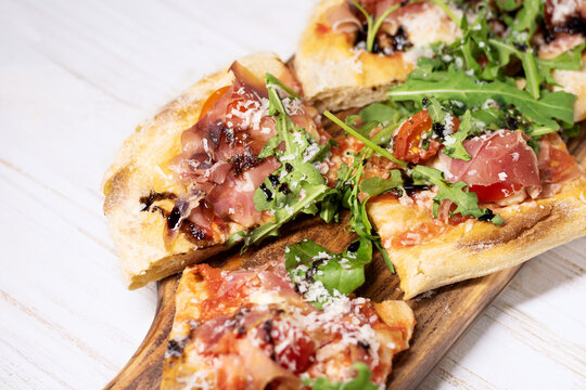 Roman pizza with prosciutto cut in pieces and served on a wooden board. Traditional roman pizza with prosciutto.