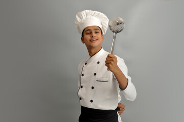 Naklejka premium Happy male chef dressed in uniform holding steel Skimmer and looking 