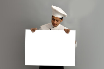 Happy male chef dressed in uniform holding white advertising banner, good poster for ad, offer or announcement, looking on board