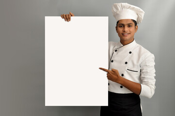 Happy male chef dressed in uniform holding white advertising banner, good poster for ad, offer or announcement, big paper billboard