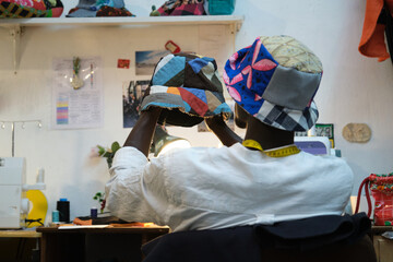 Black tailor examining the hat he is making in a sewing shop.