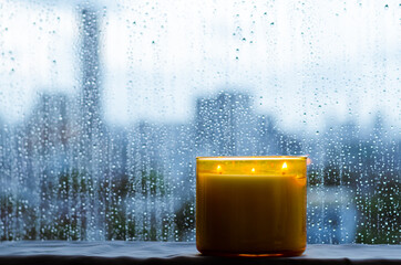 Burning aroma candle puts near by window that have rain drop in monsoon season. Zen and relax concept. - obrazy, fototapety, plakaty