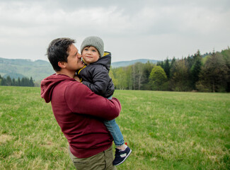 Fototapeta premium Father and son hugging on vacation on spring time meadow in mountains