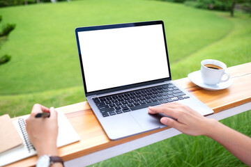 Mockup image of a woman using laptop computer with blank white desktop screen while working in the outdoors