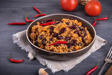 Mexican tomato rice with beans in a plate on a dark table with hot peppers
