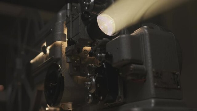 Old film projector projecting beam of light in dark room or movie theater close up.