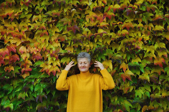 Senior woman standing outdoors against colorful natural autumn background, eyes closed.