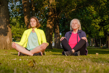 Grandmother and granddaughter meditating together in the park.