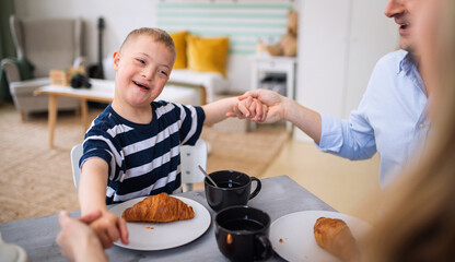 Happy down syndrome boy with parents at the table, having breakfast.