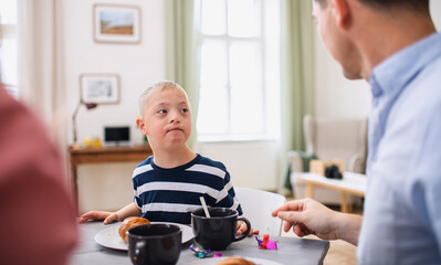 Down syndrome boy with parents at the table, having breakfast.