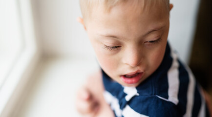 Close-up portrait of down syndrome boy indoors at home. Copy space.