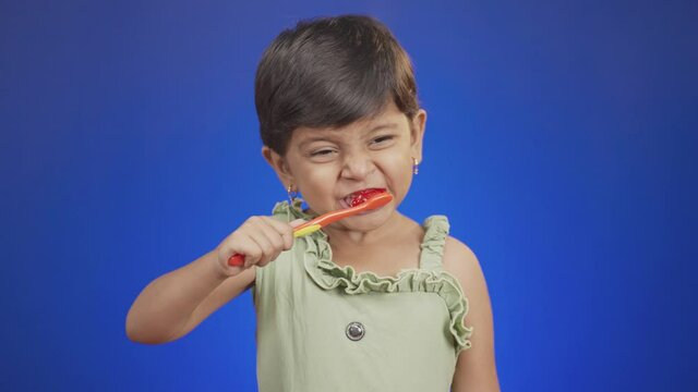 Little Girl kid brushing teeth on blue color background - concept of childrens dental healthcare by cleaning daily