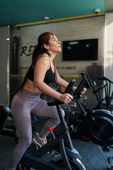 Fototapeta na wymiar young latina woman using the bike machine inside the gym, vertical orientation