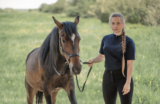 Young woman, 20 years old, is standing next to her horse in outdoors. Horse rider and her trotter are in outside.