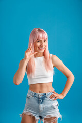 Playful young woman with pink hair laughing at camera, standing isolated over blue studio background. Emotions, lifestyle concept